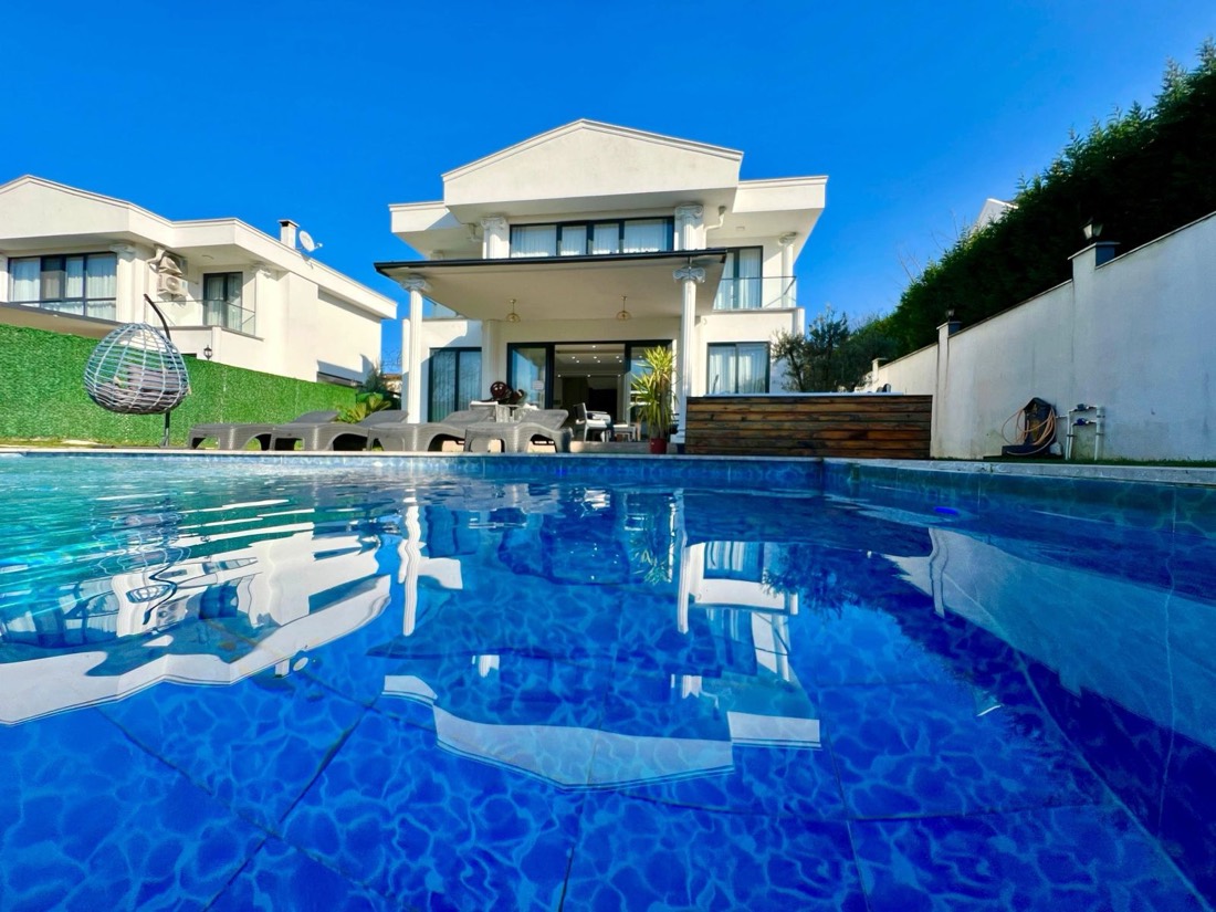 Havuzdan villa cephesi, şezlonglar ve masmavi gökyüzü